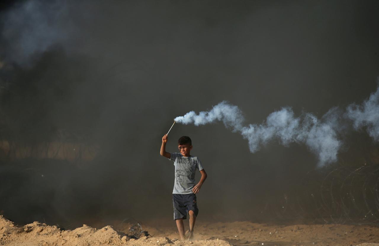 Palestinian boy holds a tear gas canister fired by Israeli troops during a protest at the Israel-Gaza border fence in the southern Gaza Strip