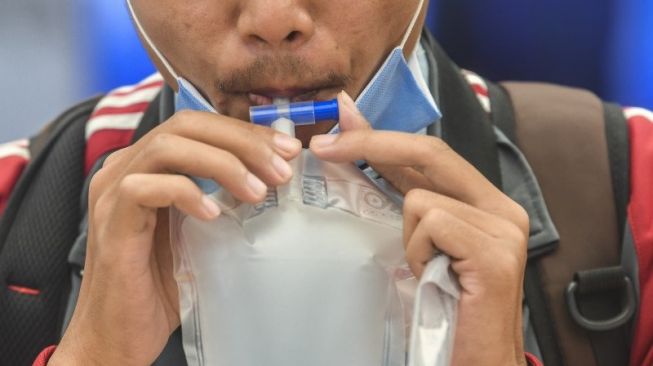 Calon penumpang mengembuskan nafas ke dalam kantong untuk dites COVID-19 dengan GeNose C19