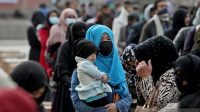 Seorang perempuan Afghanistan menggendong anaknya di tengah orang-orang yang menunggu paket bantuan yang disalurkan oleh sebuah kelompok bantuan kemanusiaan Turki